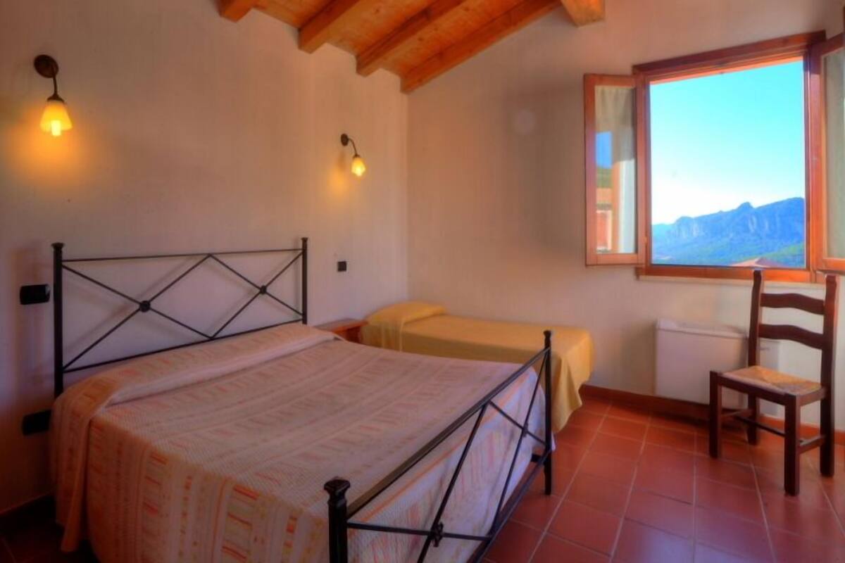 Ein Schlafzimmer mit einem Bett, einem Sessel, einem Fenster mit Bergblick und zwei Wandleuchten.