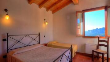 A bedroom with a bed, a chair, a window with a mountain view, and two wall-mounted lights.