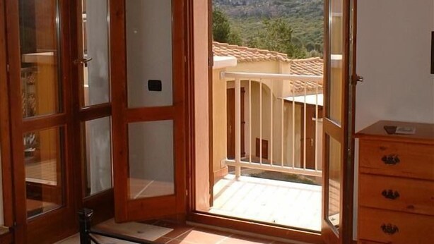 Una habitación con techo de madera, una puerta corrediza de vidrio que da a un balcón con vistas a montañas y un aparador de madera.