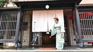 A person in traditional attire standing at the entrance of a building with a large banner and a traditional Japanese gate.