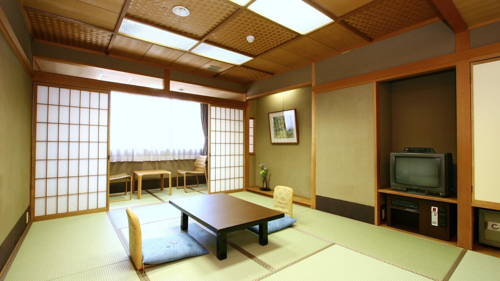 A traditional Japanese-style room with tatami flooring, a low table, a television, and sliding doors.
