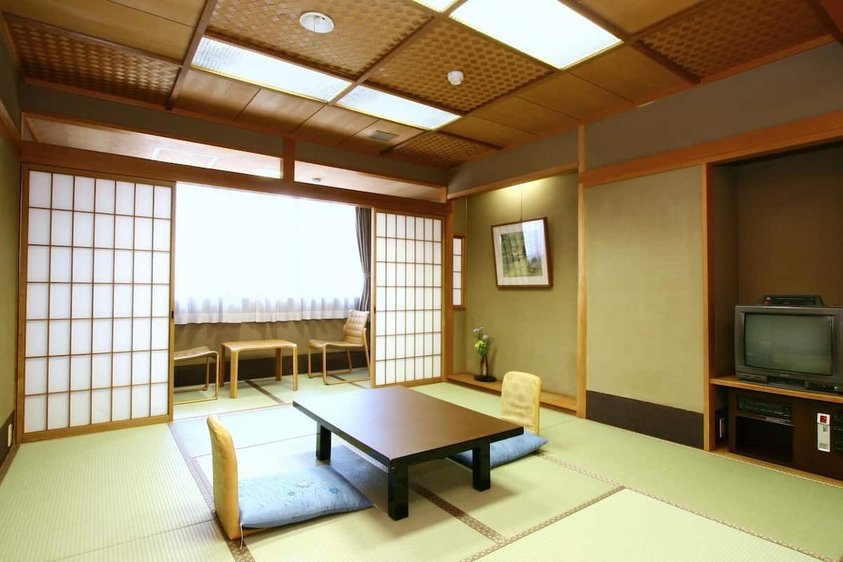 A traditional Japanese-style room with tatami flooring, a low table, a television, and sliding doors.