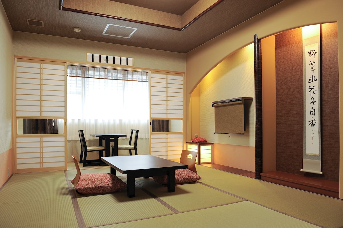 A traditional Japanese room with tatami flooring, a low table, chairs, and sliding doors.