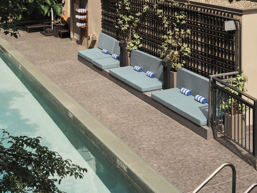 A poolside area with a long pool, lounge chairs, and a tiled walkway.