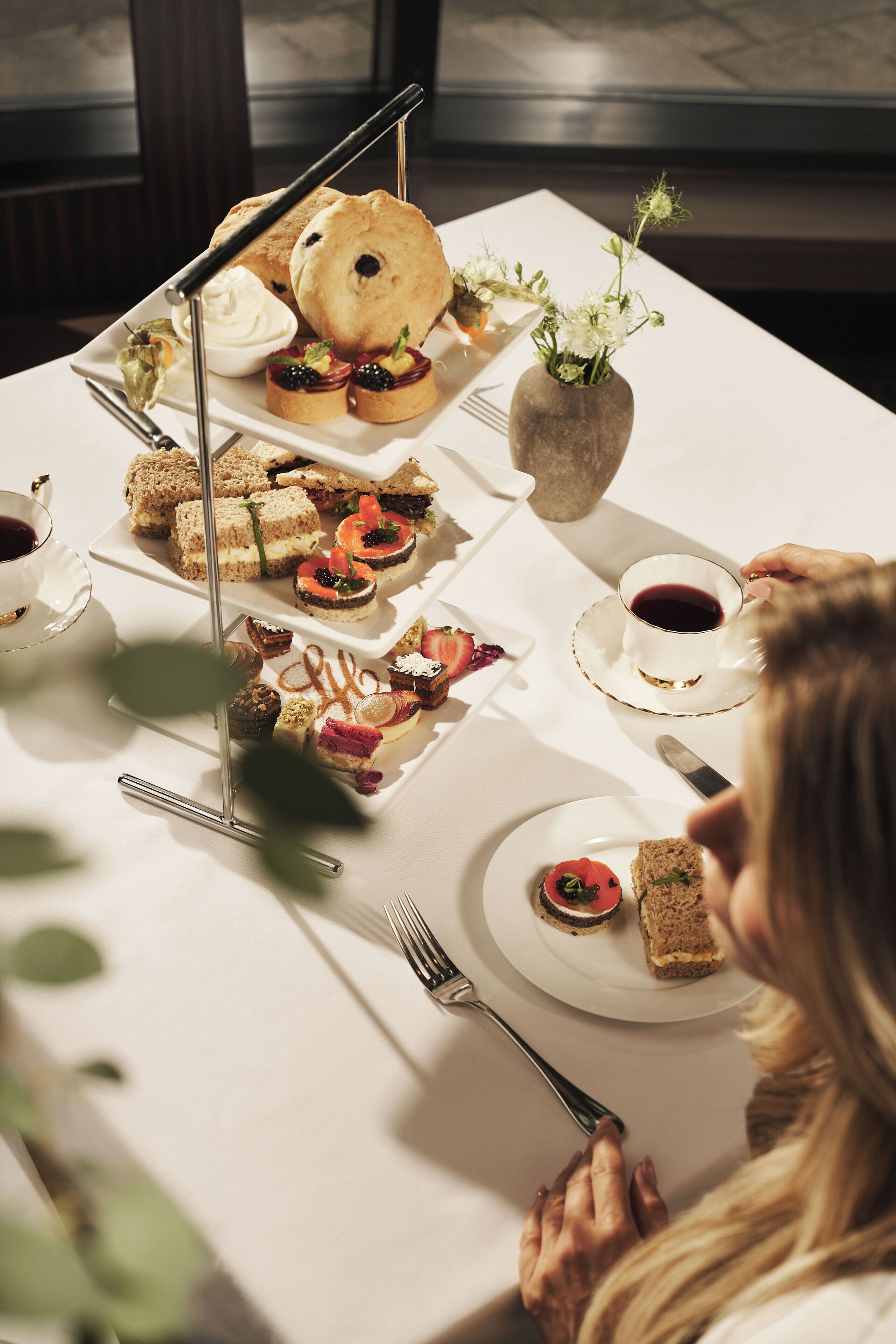 A table set with various food items, including sandwiches, pastries, and a vase with flowers.