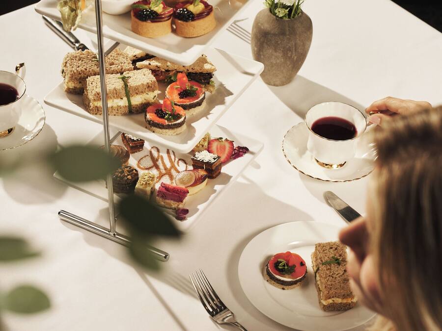 A table set with various food items, including sandwiches, pastries, and a vase with flowers.