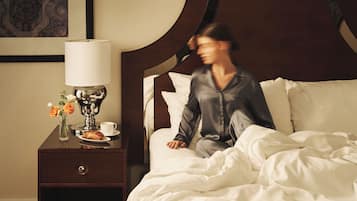 A hotel room with a bed, a nightstand with a lamp, a cup, and a plate with a pastry.