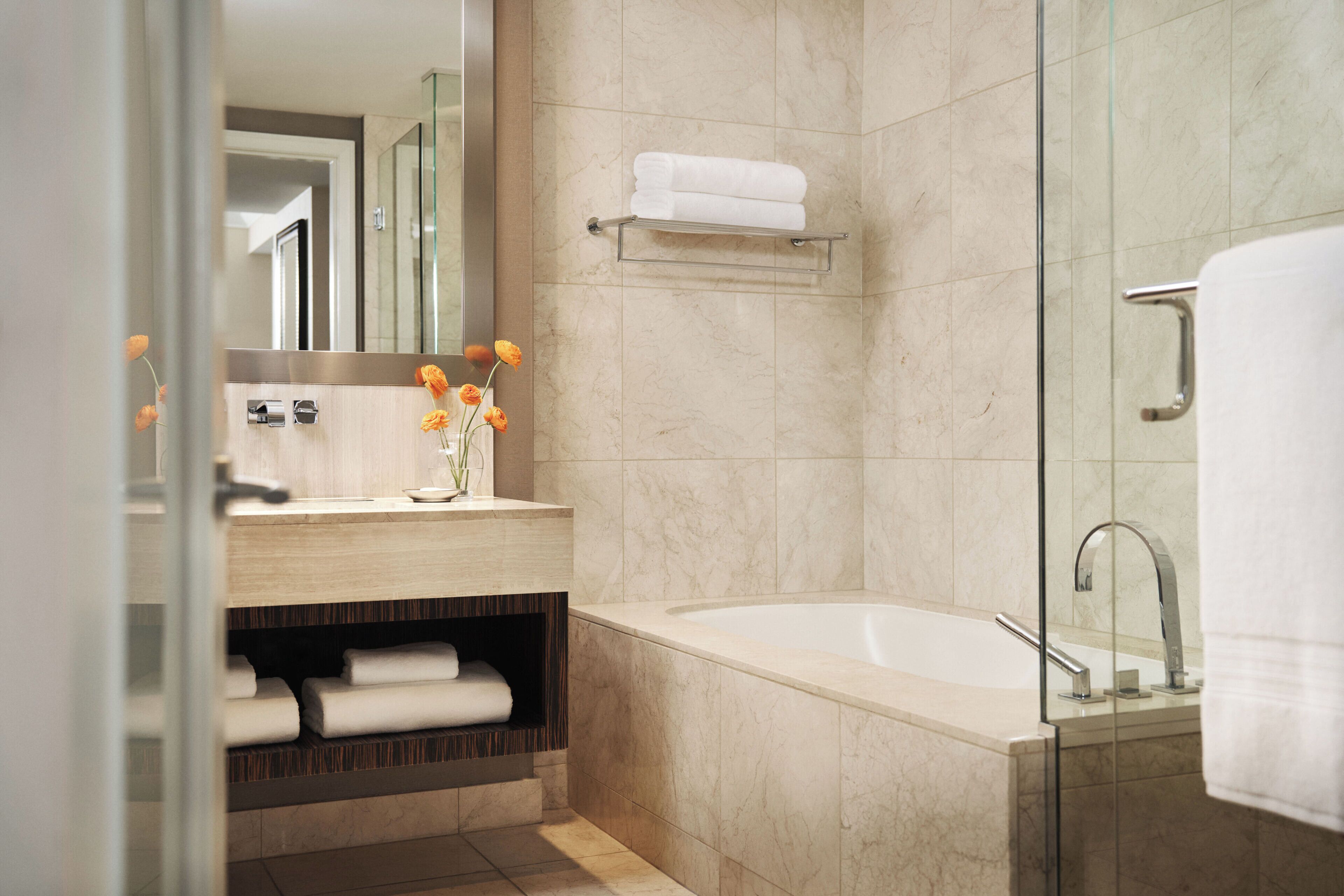 A modern bathroom with a bathtub, a glass shower enclosure, a vanity with a mirror, and a shelf with towels.