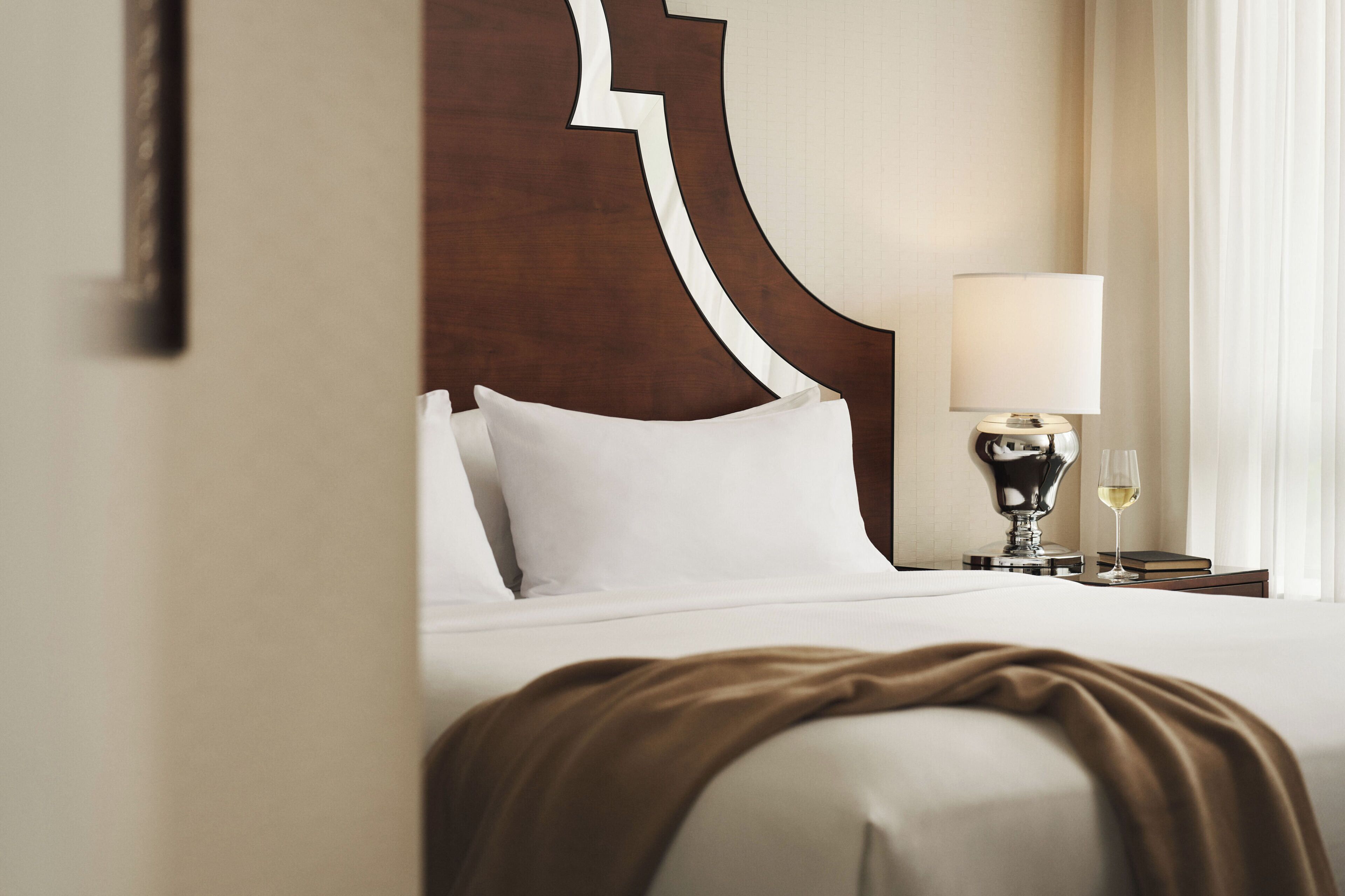 Ein Hotelzimmer mit Bett, Nachttisch mit Lampe und einem Weinglas.