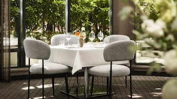 A table set for four with a white tablecloth, four grey upholstered chairs, and a vase with flowers.