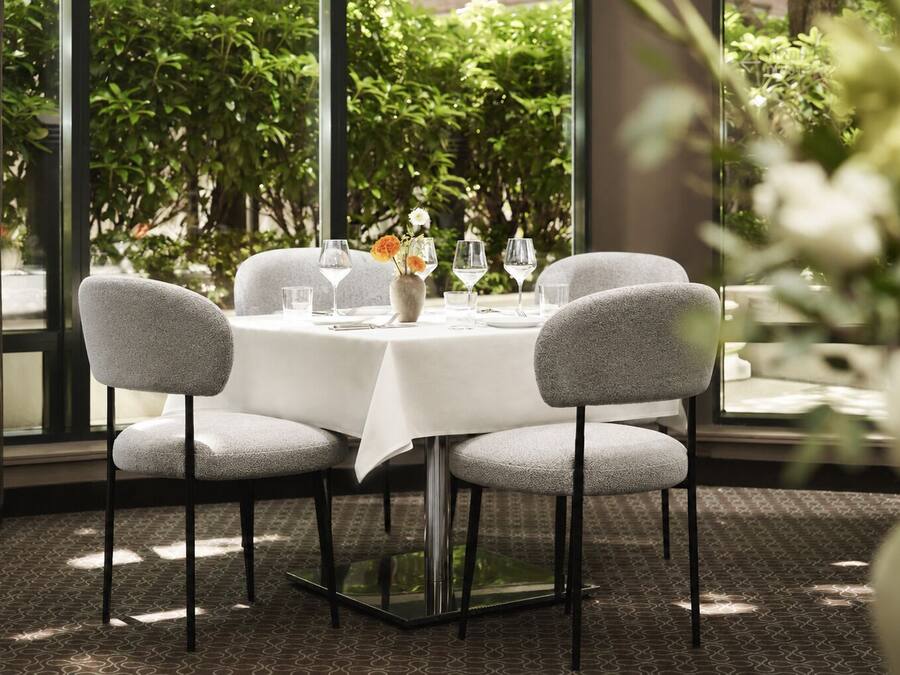 A table set for four with a white tablecloth, four grey upholstered chairs, and a vase with flowers.