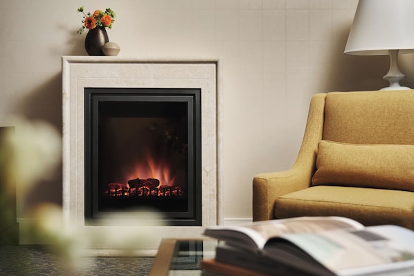 A fireplace with a fire, a sofa, and a lamp.