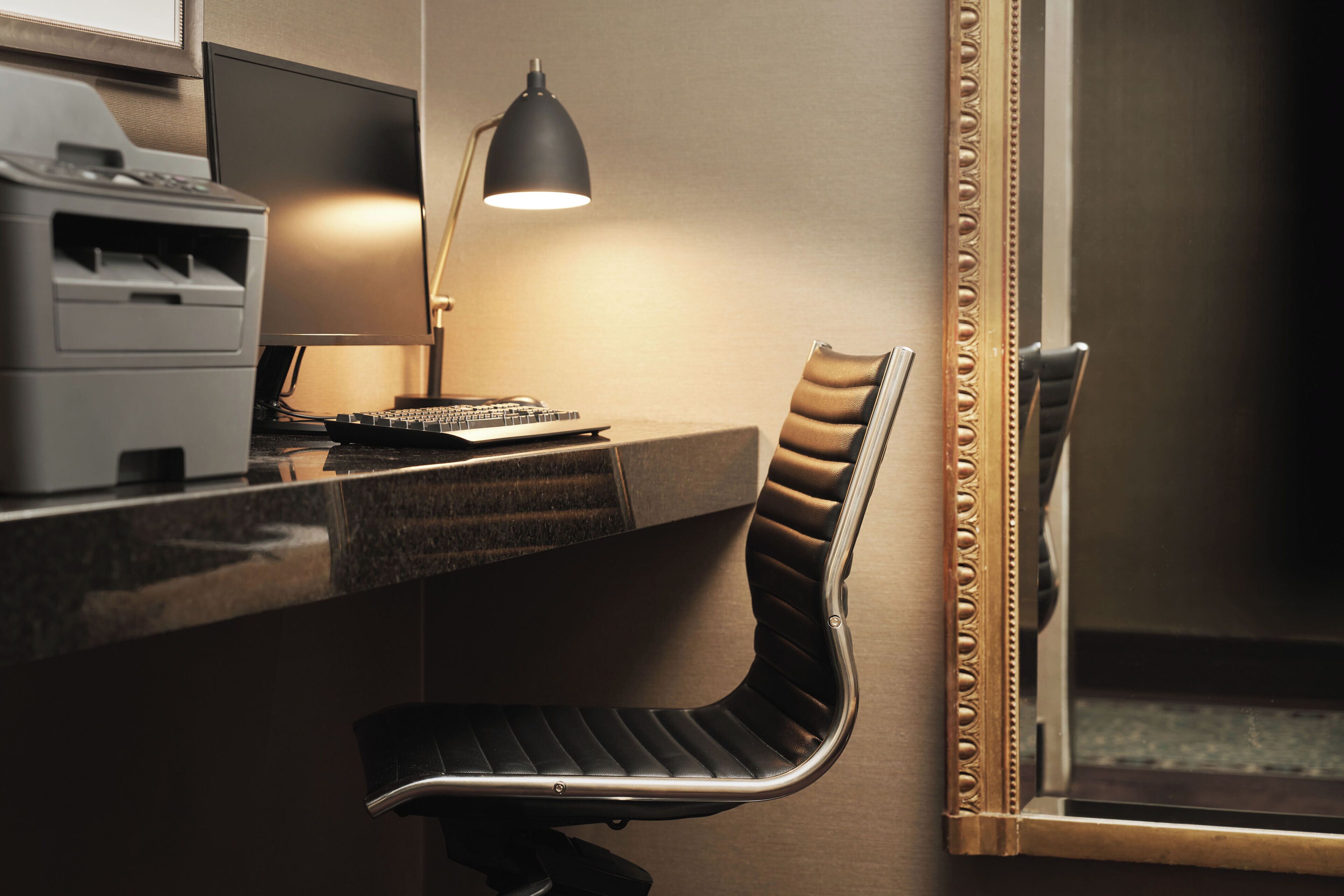 A modern office desk with a computer, a lamp, and a chair.