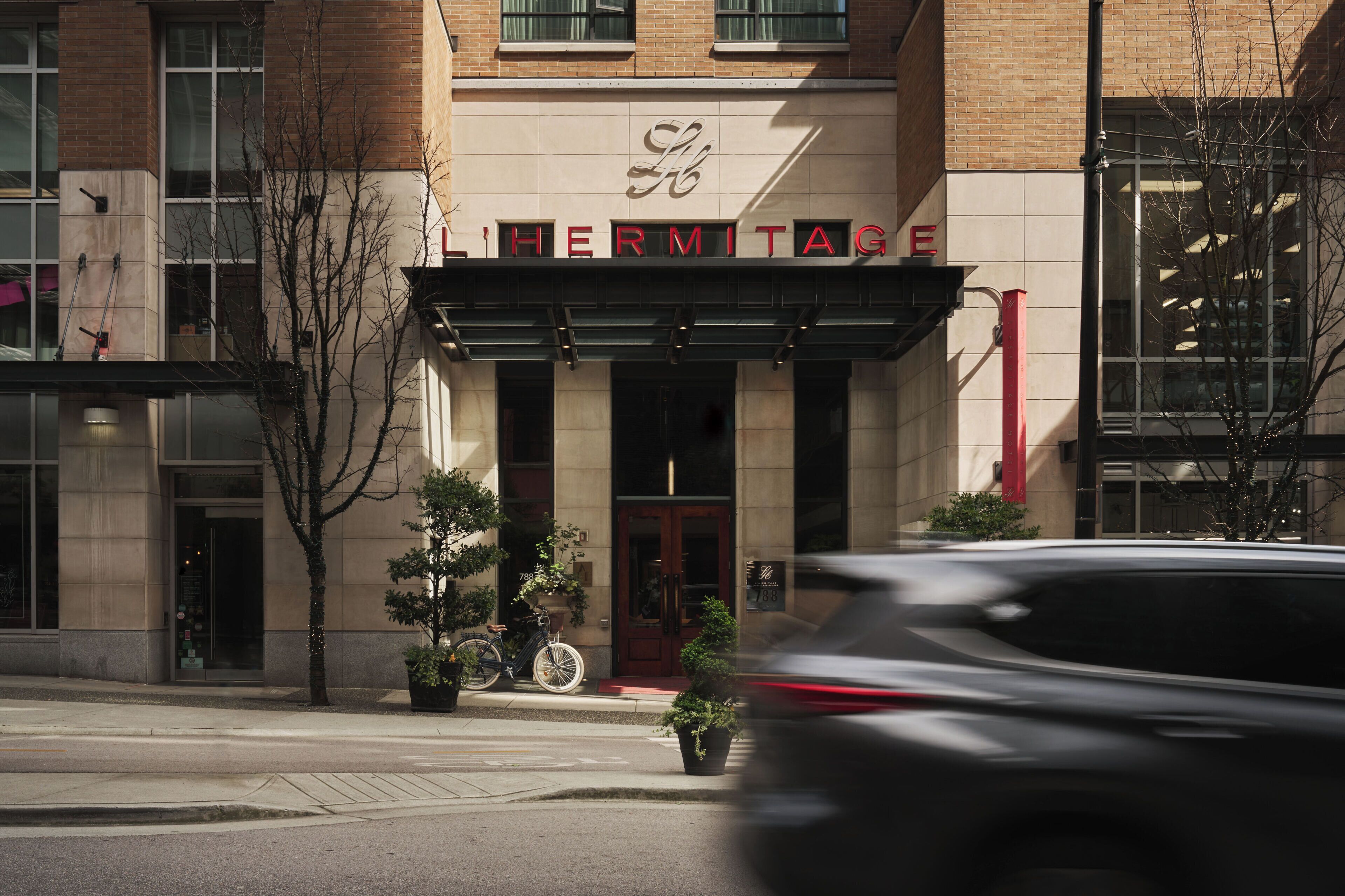 A building with a sign reading 'HERMITAGE' and a large entrance. There are potted plants and a bicycle parked outside.