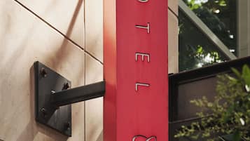 Ein rotes Hotelschild mit dem Schriftzug 'HOTEL' und einem Logo, das an einer Wand mit einer Metallhalterung befestigt ist.