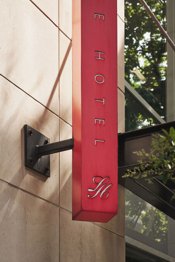 A red hotel sign with the name 'HOTEL' and a logo, mounted on a wall with a metal bracket.