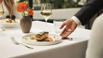 A dining table with a plate of food, a glass of white wine, and a vase with flowers.