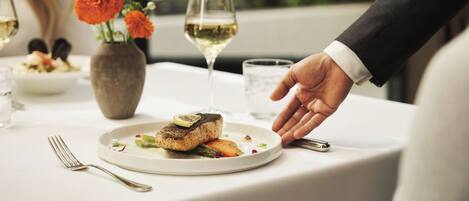 A dining table with a plate of food, a glass of white wine, and a vase with flowers.