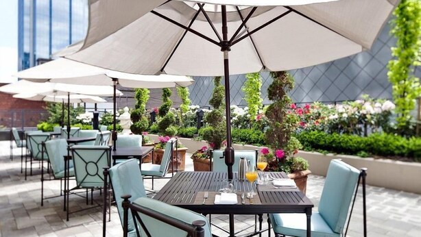 An outdoor seating area with tables and chairs, umbrellas, and potted plants.