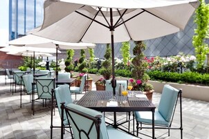 An outdoor seating area with tables and chairs, umbrellas, and potted plants.