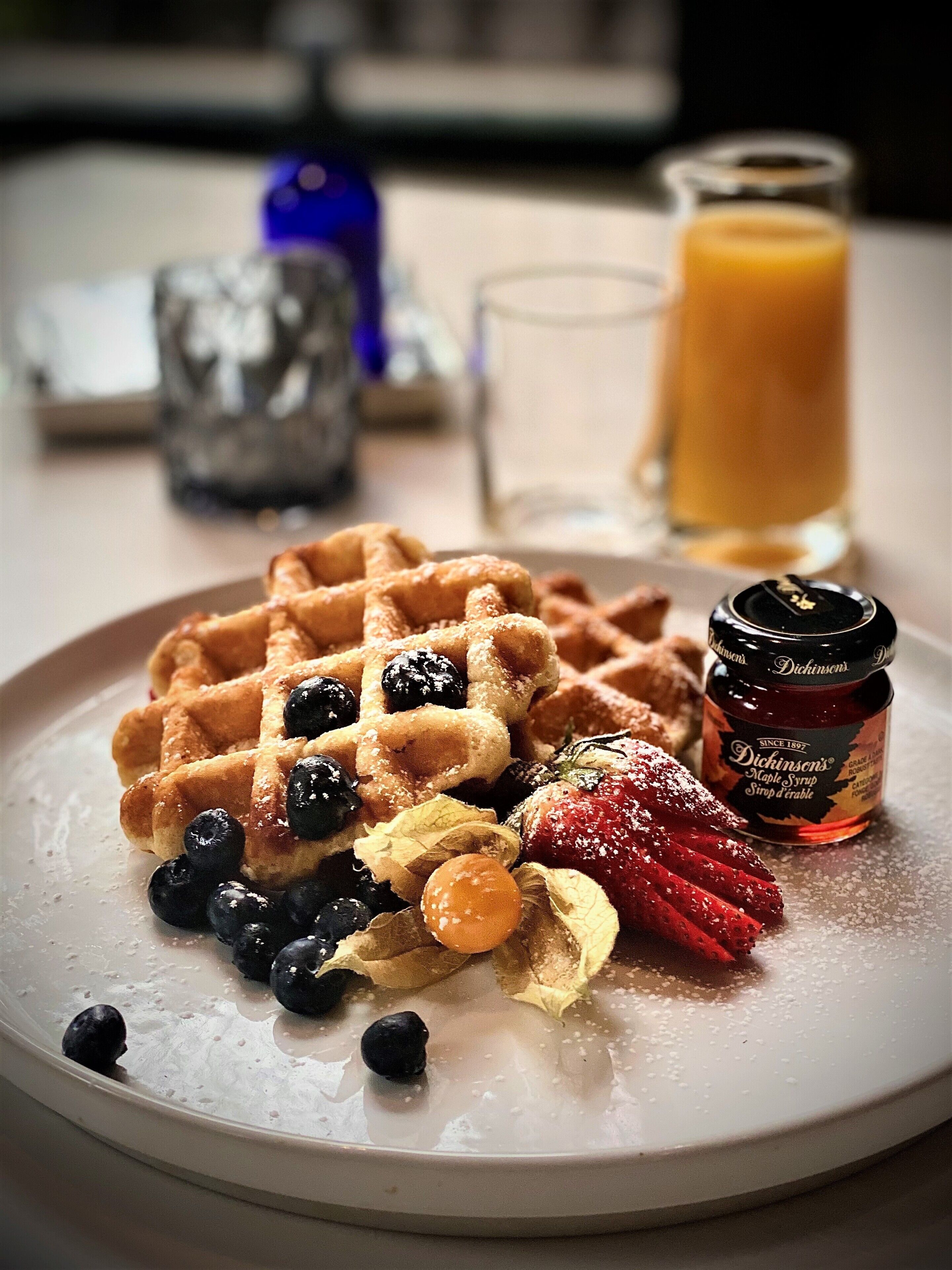 Um prato com waffles, amoras, morangos e um pote de xarope.
