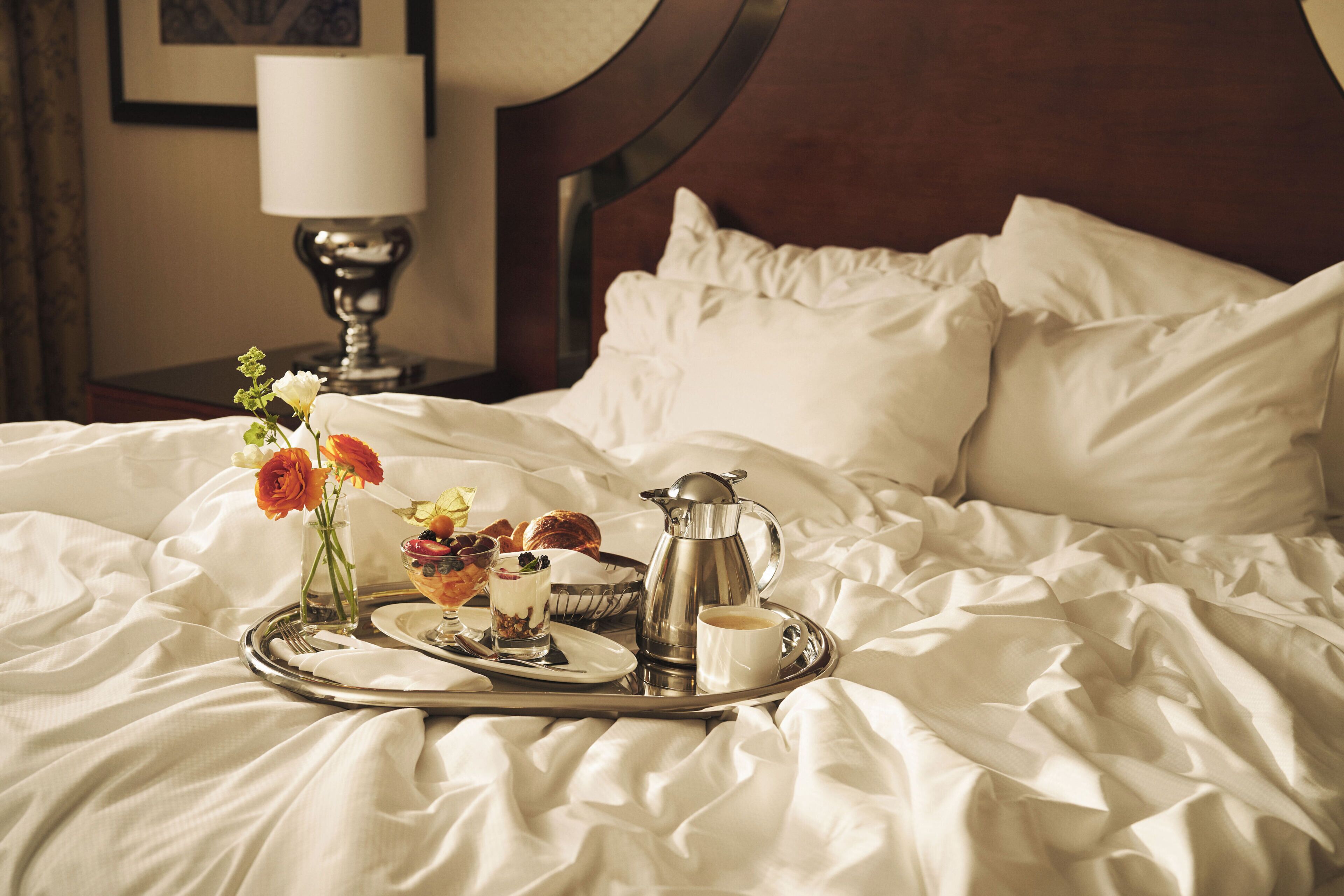A neatly made bed with a tray of breakfast items including pastries, a coffee pot, and a cup of coffee.