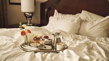 A neatly made bed with a tray of breakfast items including pastries, a coffee pot, and a cup of coffee.