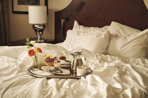A neatly made bed with a tray of breakfast items including pastries, a coffee pot, and a cup of coffee.