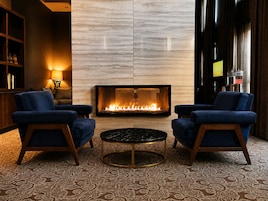 A modern lounge area with a fireplace, two blue armchairs, a round coffee table, and a patterned carpet.