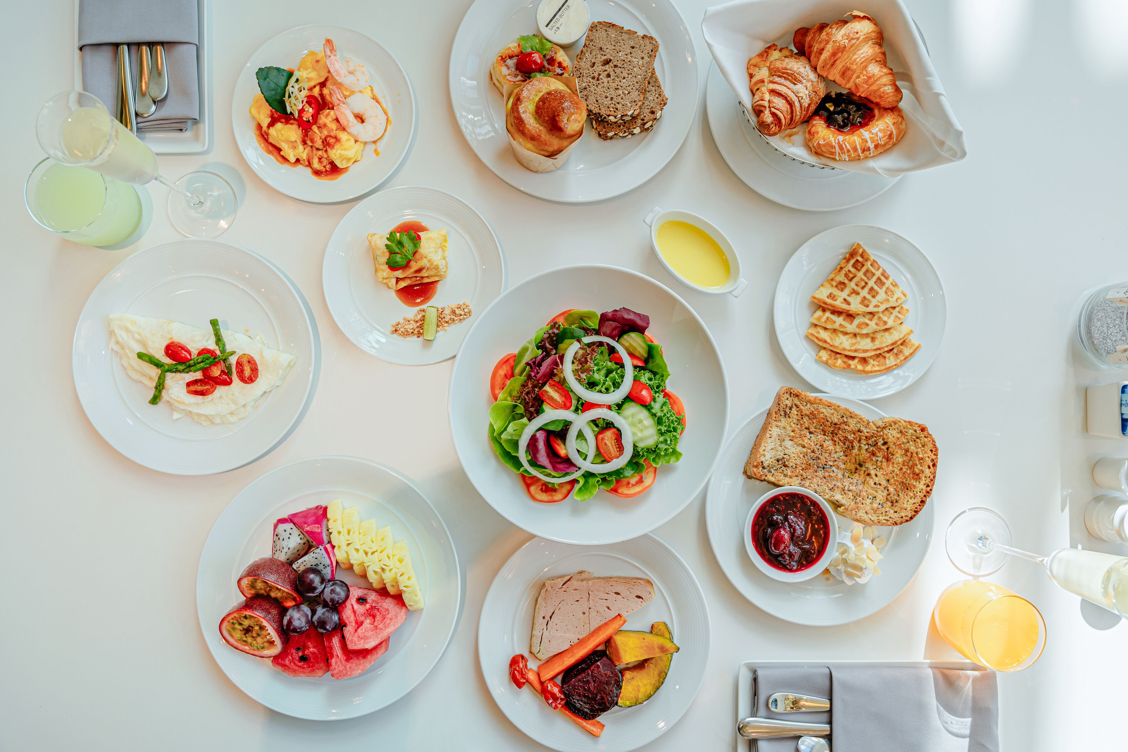 A breakfast buffet with various dishes, including fruits, vegetables, bread, and pastries.