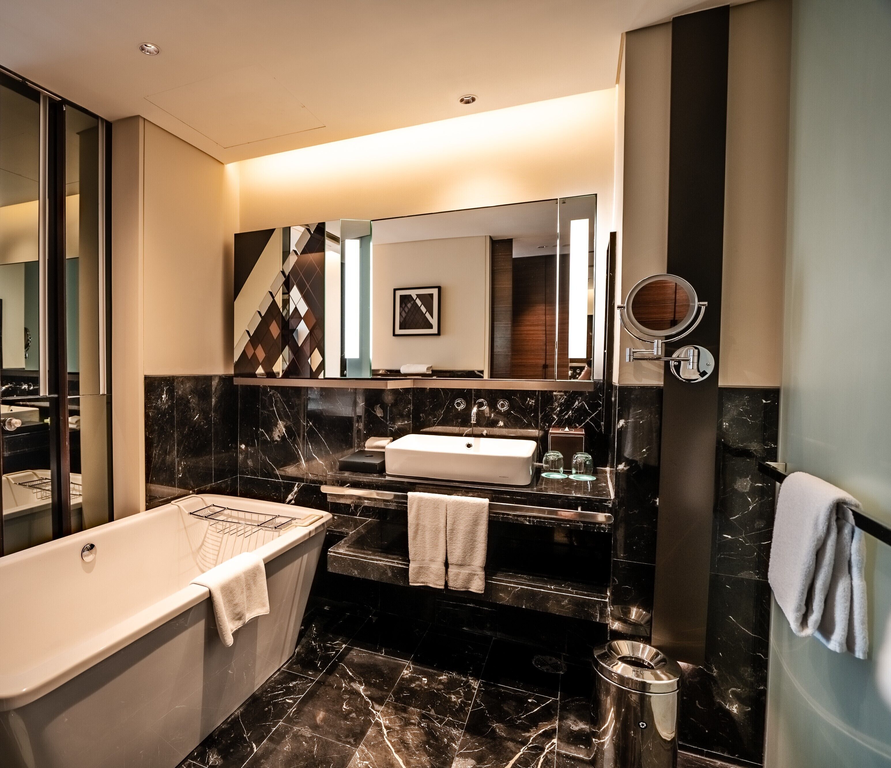 A modern bathroom with a freestanding bathtub, a vanity with a mirror, and a marble backsplash.