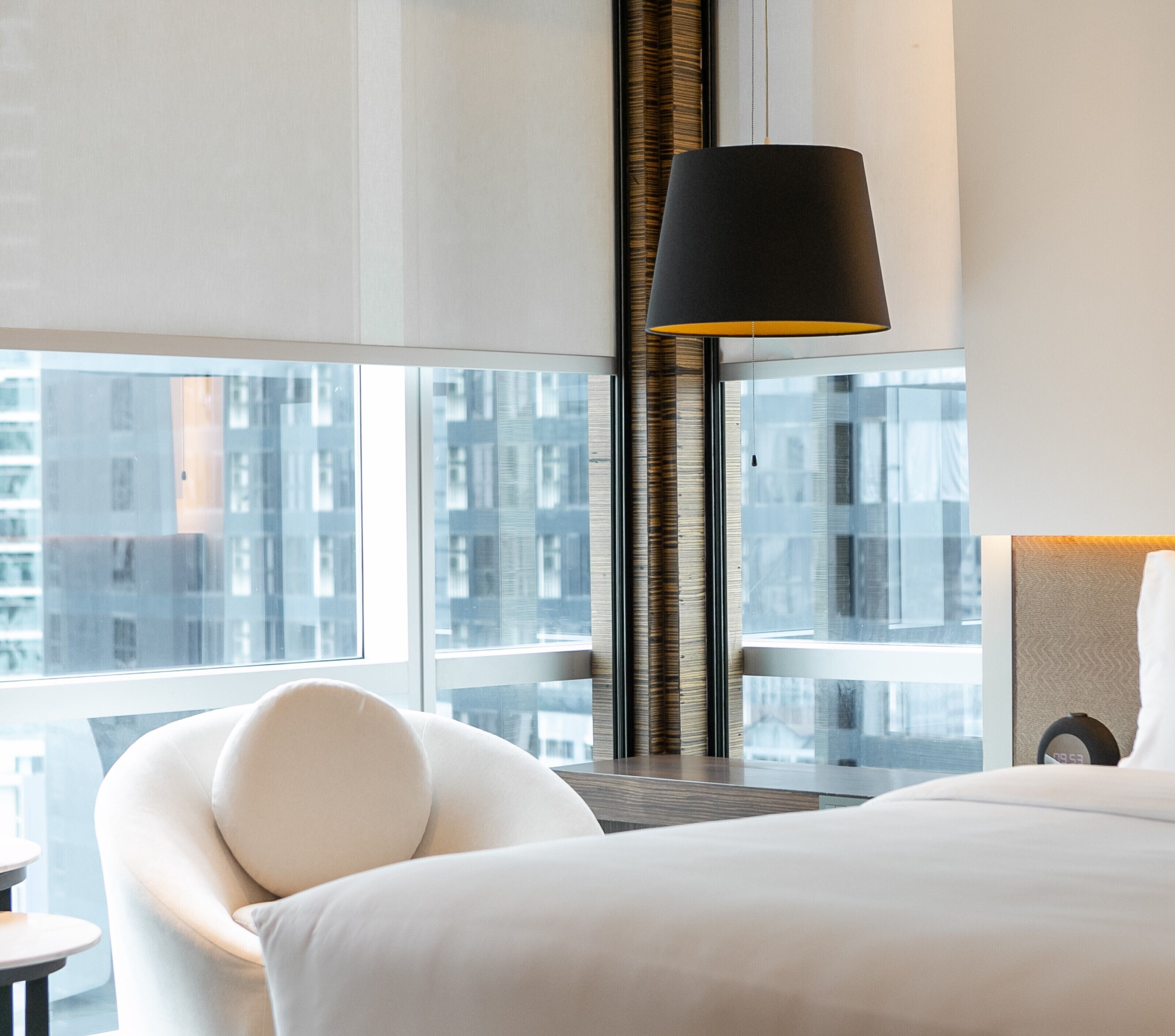 Habitación de hotel moderna con una cama grande, un sillón blanco, un escritorio y un ventanal con vistas a la ciudad.