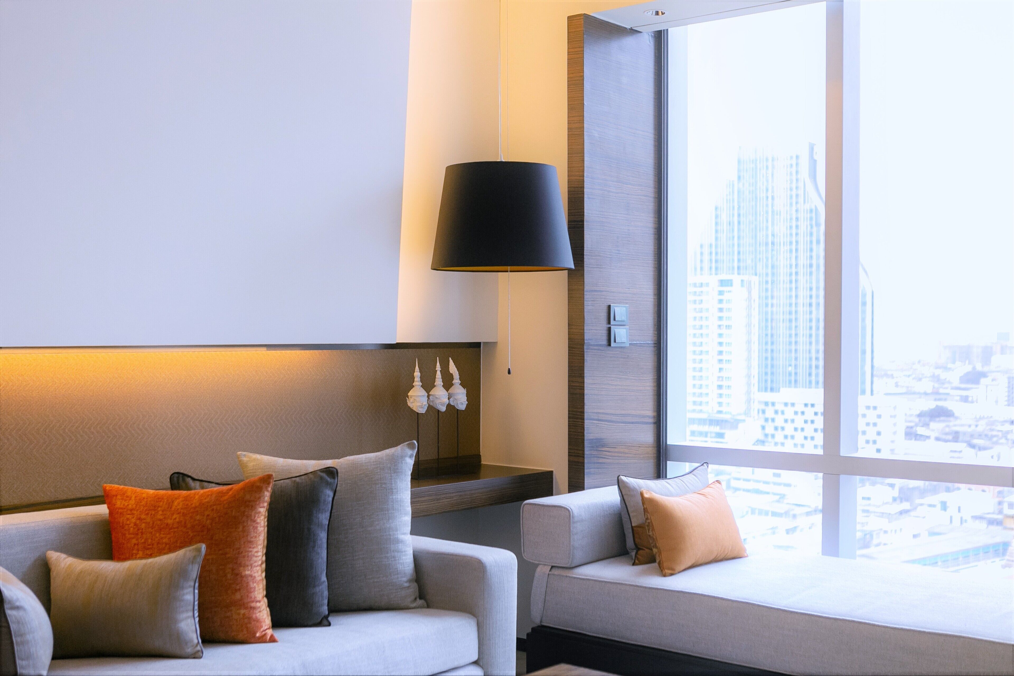 Una habitación de hotel moderna con un sofá, una lámpara y vistas a la ciudad a través de amplios ventanales.