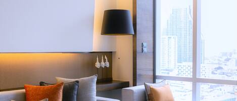 Una habitación de hotel moderna con un sofá, una lámpara y vistas a la ciudad a través de amplios ventanales.