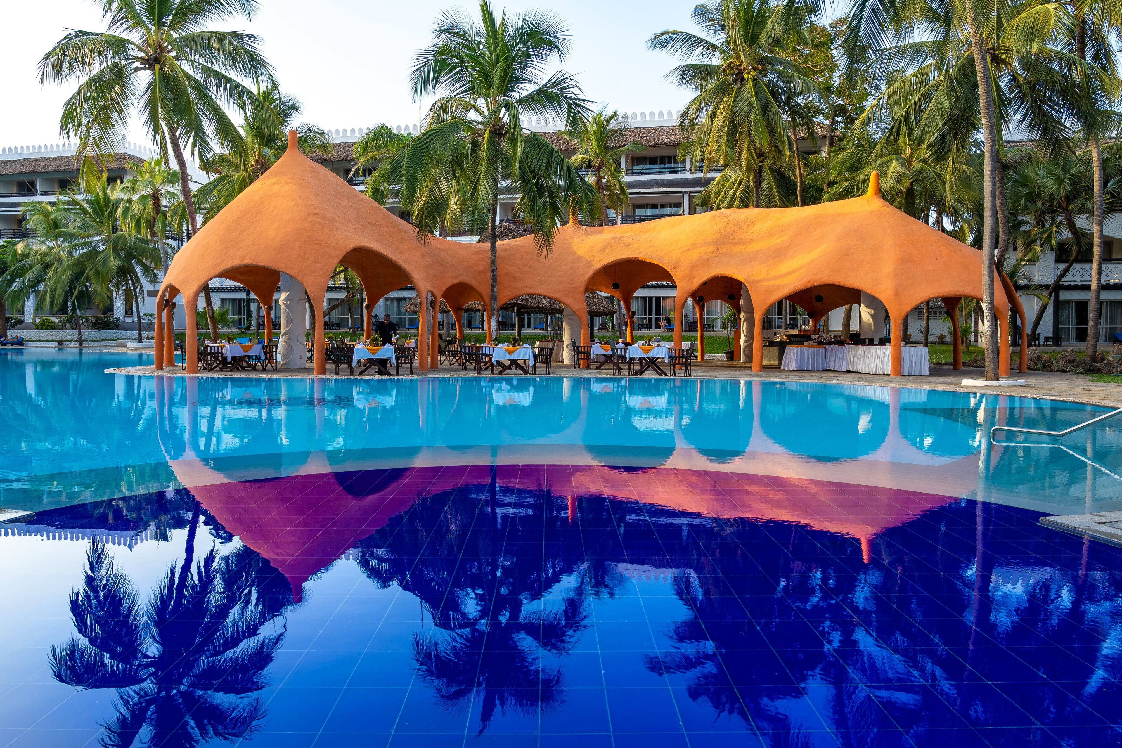 Un área de piscina con zona de estar cubierta y palmeras.