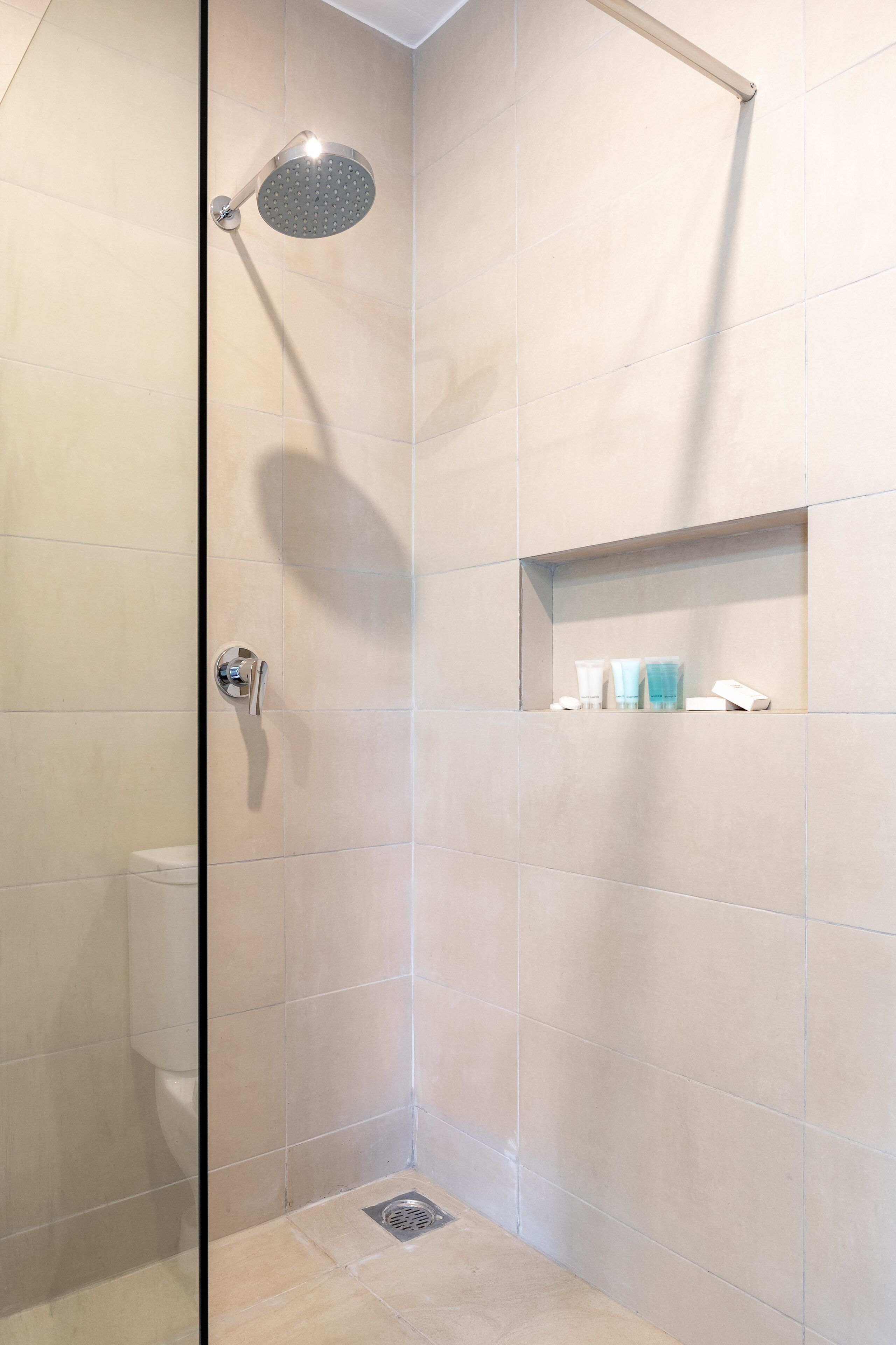 Een moderne badkamer met een douche, toilet en een plank met toiletartikelen.