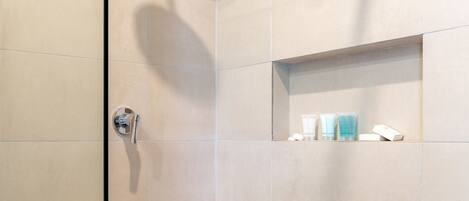 Une salle de bain moderne équipée d’une douche, de toilettes et d’une étagère où sont rangés les articles de toilette.