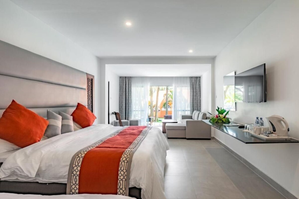 A modern hotel room with a large bed, a seating area, a flat-screen TV, and a kitchenette.