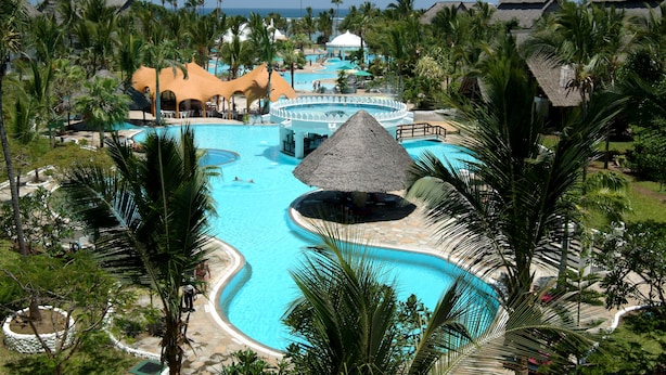 A resort with multiple swimming pools, palm trees, and thatched-roof structures. - Southern Palms Beach Resort (Diani Beach)