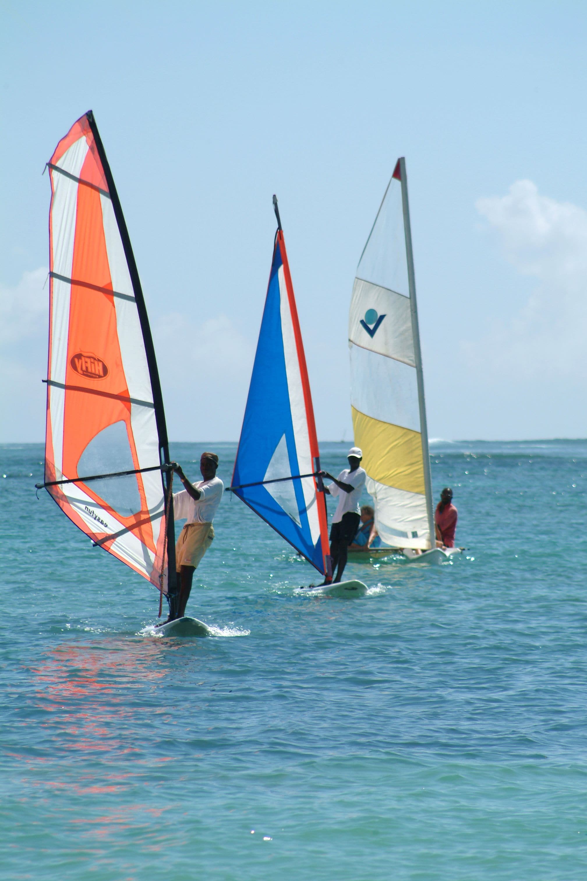 Three people windsurfing on a calm sea.