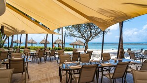 An outdoor dining area with tables and chairs, a view of the beach, and palm trees. - Southern Palms Beach Resort (Diani Beach)