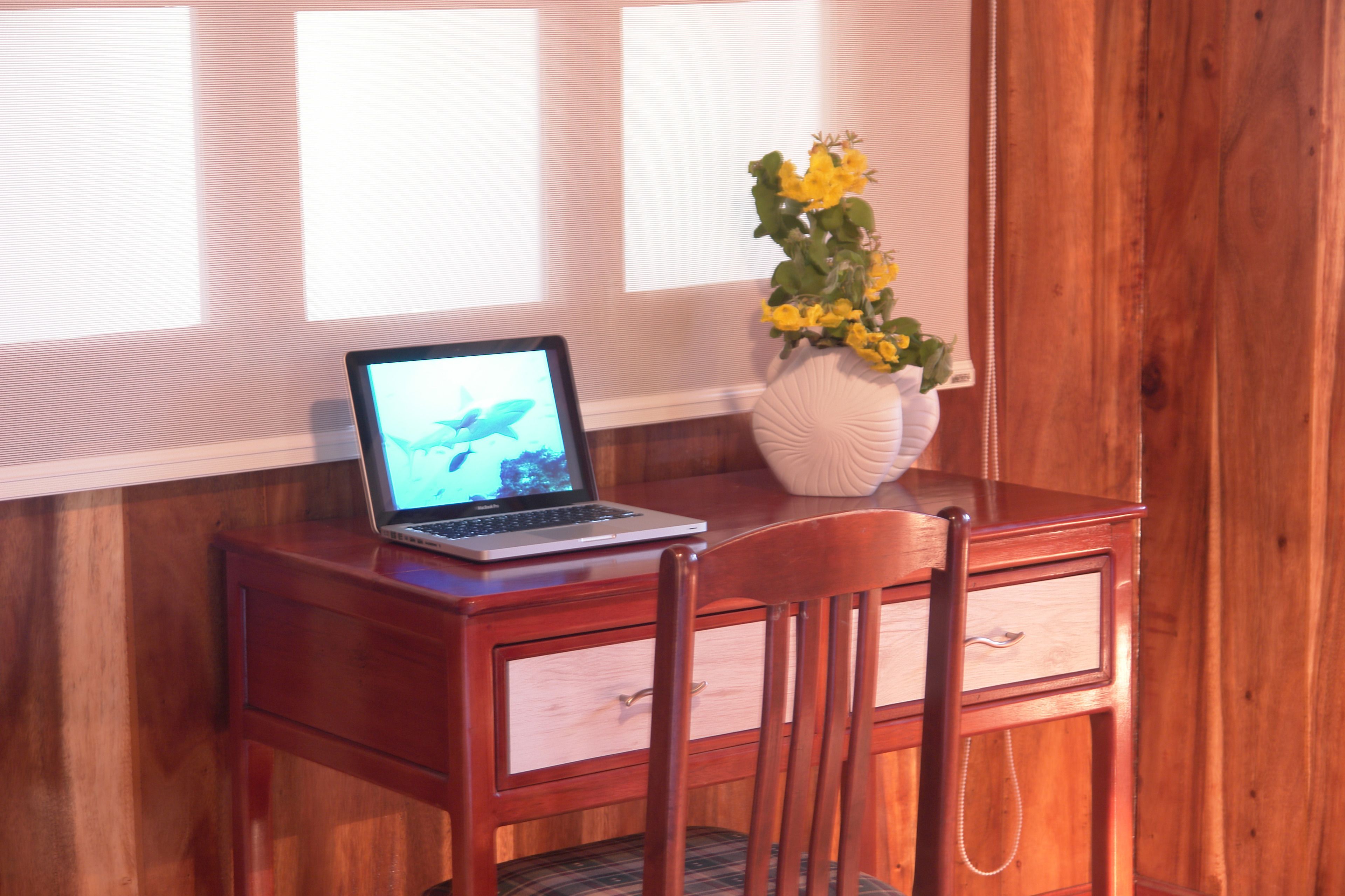 A wooden desk with a laptop, a vase with yellow flowers, and a chair.