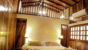 Habitación de hotel con decoración de madera, una cama con almohadas, una mesita de noche y una ventana con barrotes.