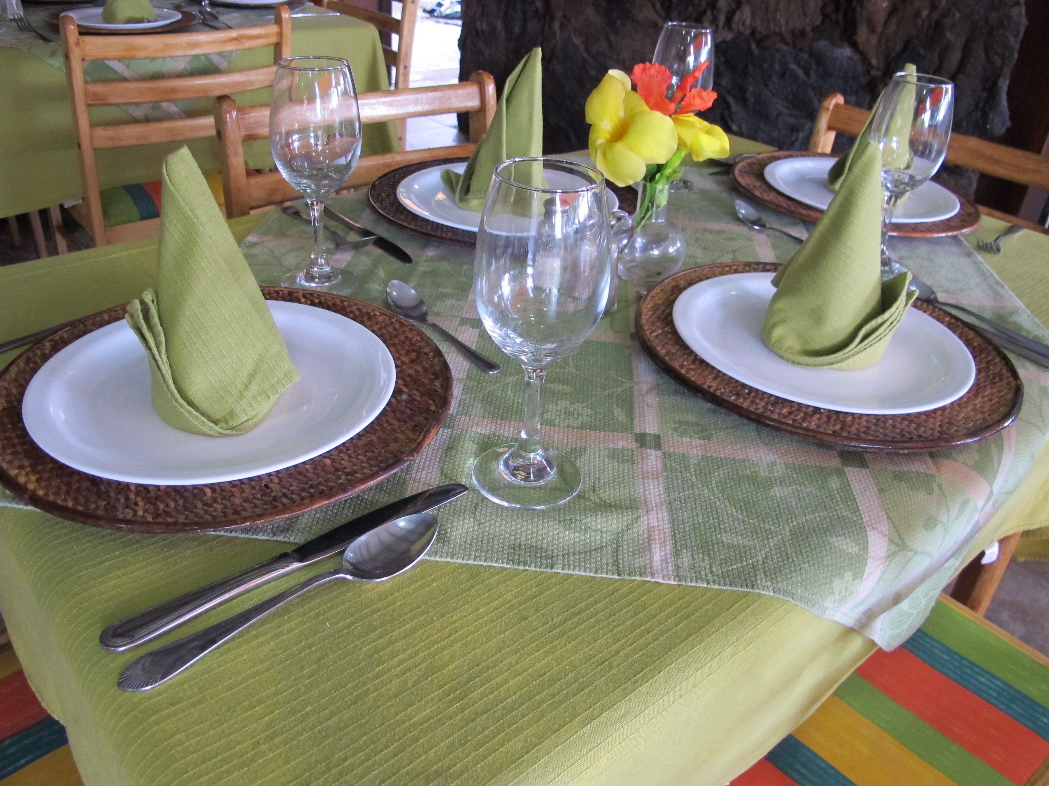 Una mesa de comedor puesta con servilletas verdes, platos blancos y cristalería transparente.