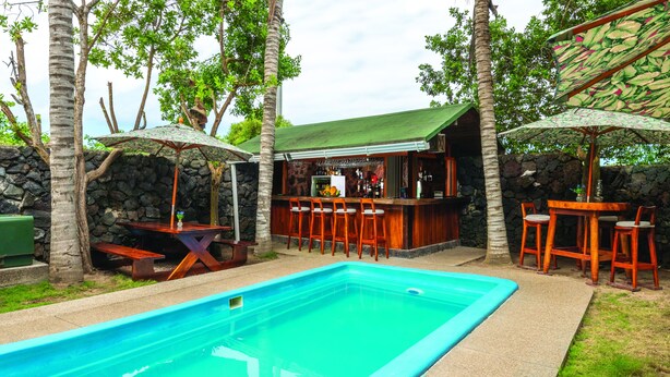 Zona de bar junto a la piscina, con pared de piedra, mostrador de madera y taburetes.