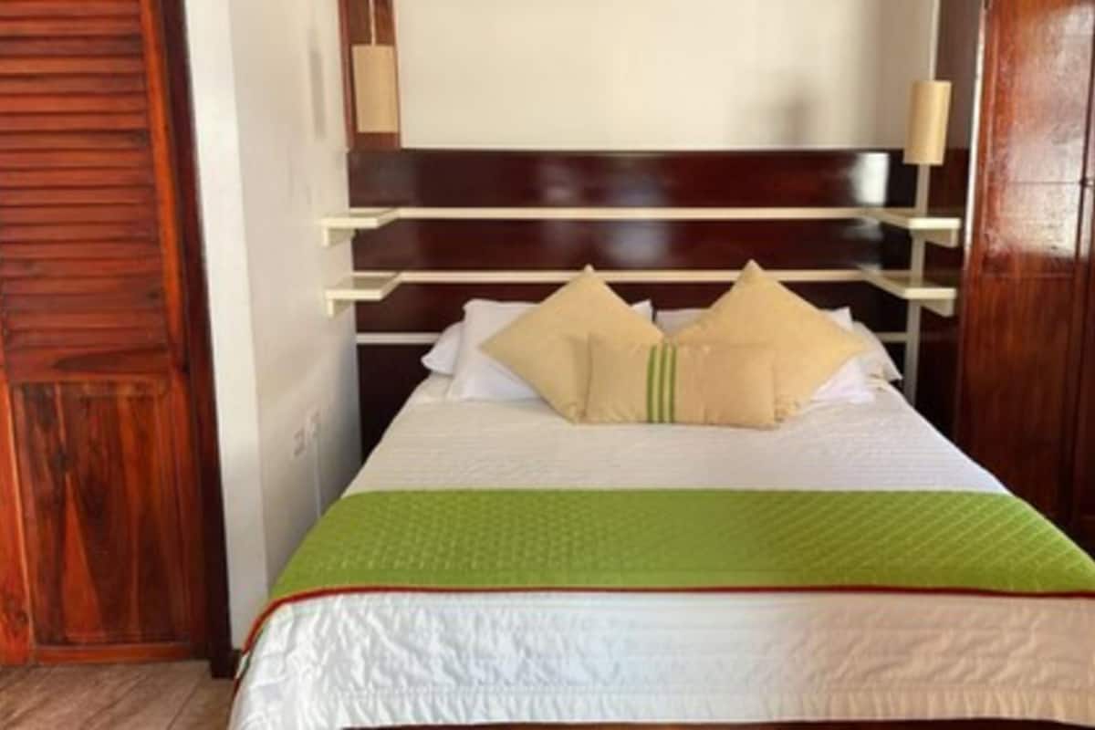 Una cama bien hecha con colcha verde y blanca, dos almohadas color beige y un cabecero de madera.