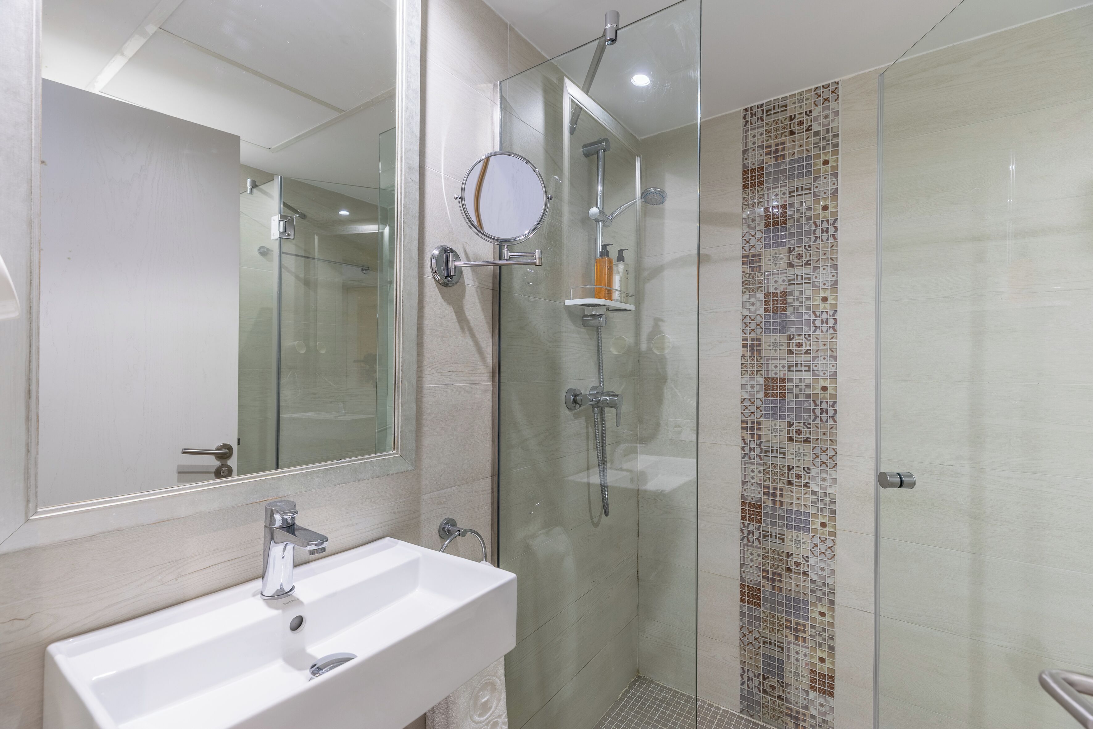 A modern bathroom with a glass-enclosed shower, a large mirror, and a white sink.