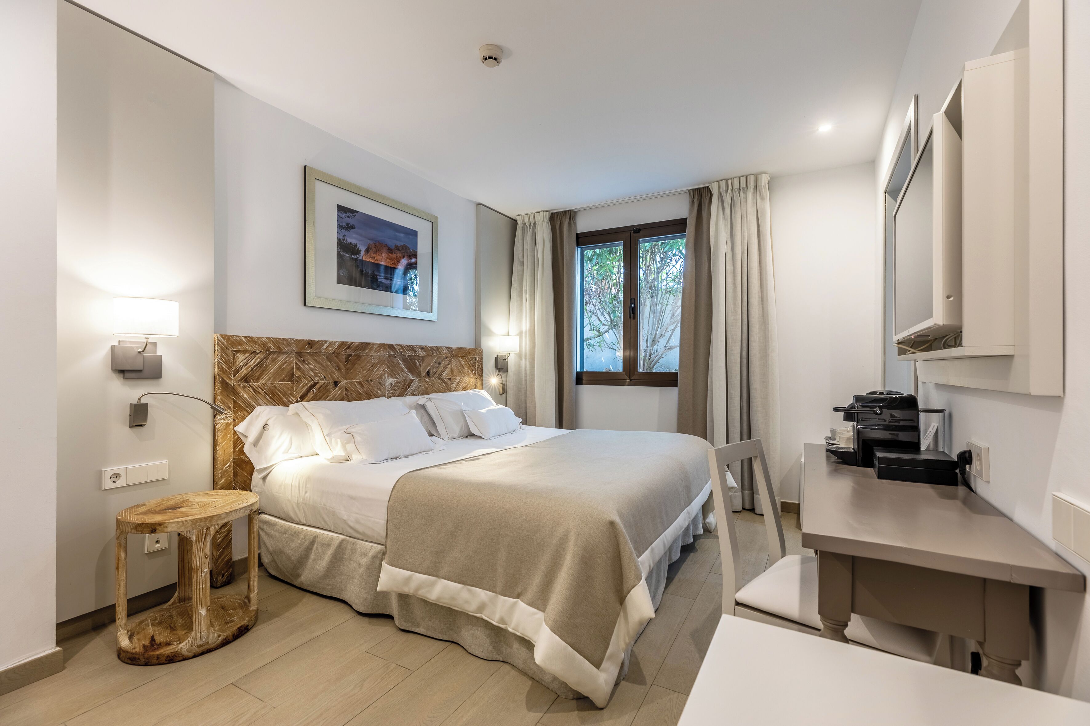 Une chambre d’hôtel avec un lit, une table de chevet, un bureau et une fenêtre avec des rideaux.