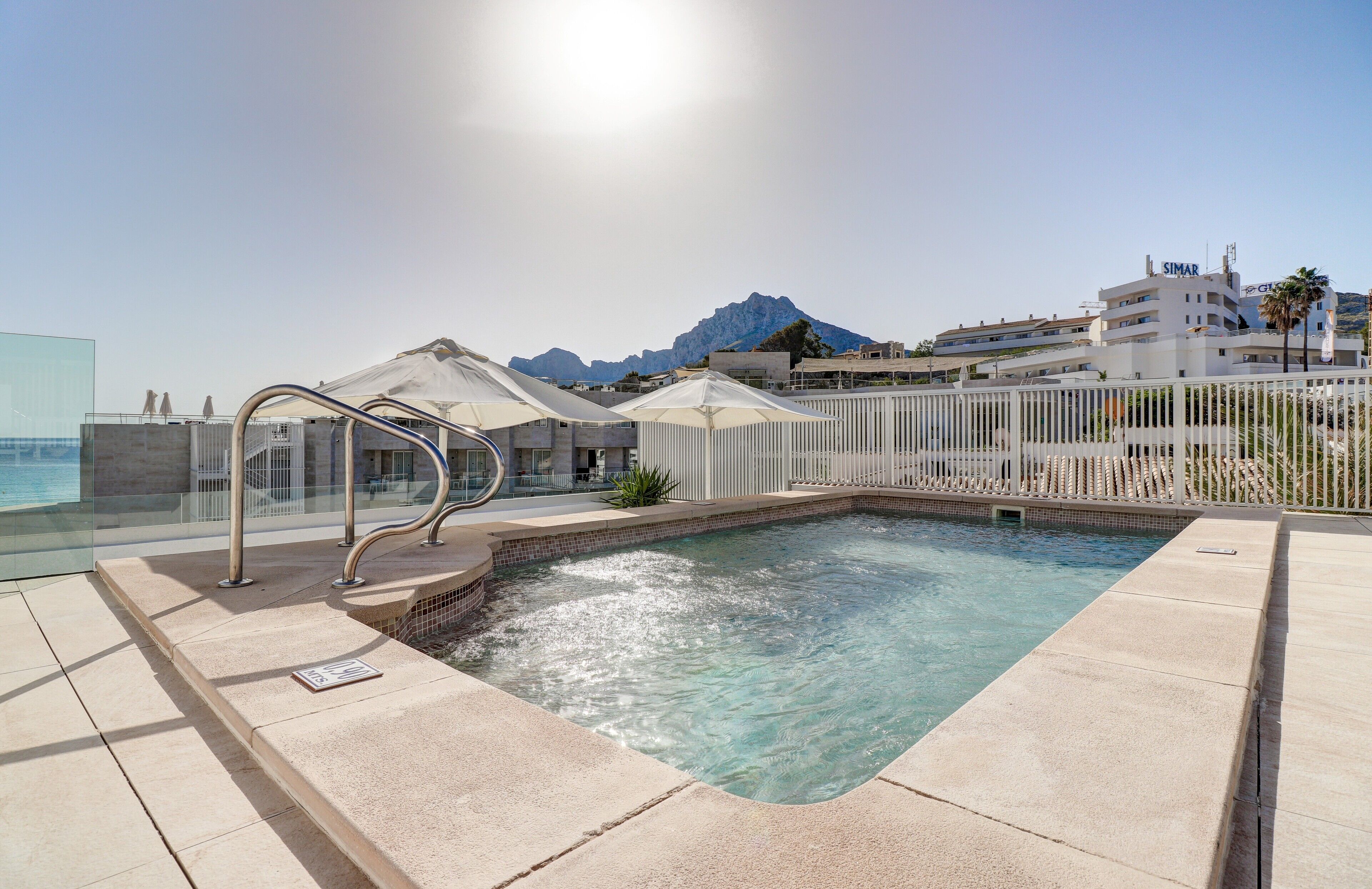 A pool area with clear water, a metal ladder, and umbrellas.