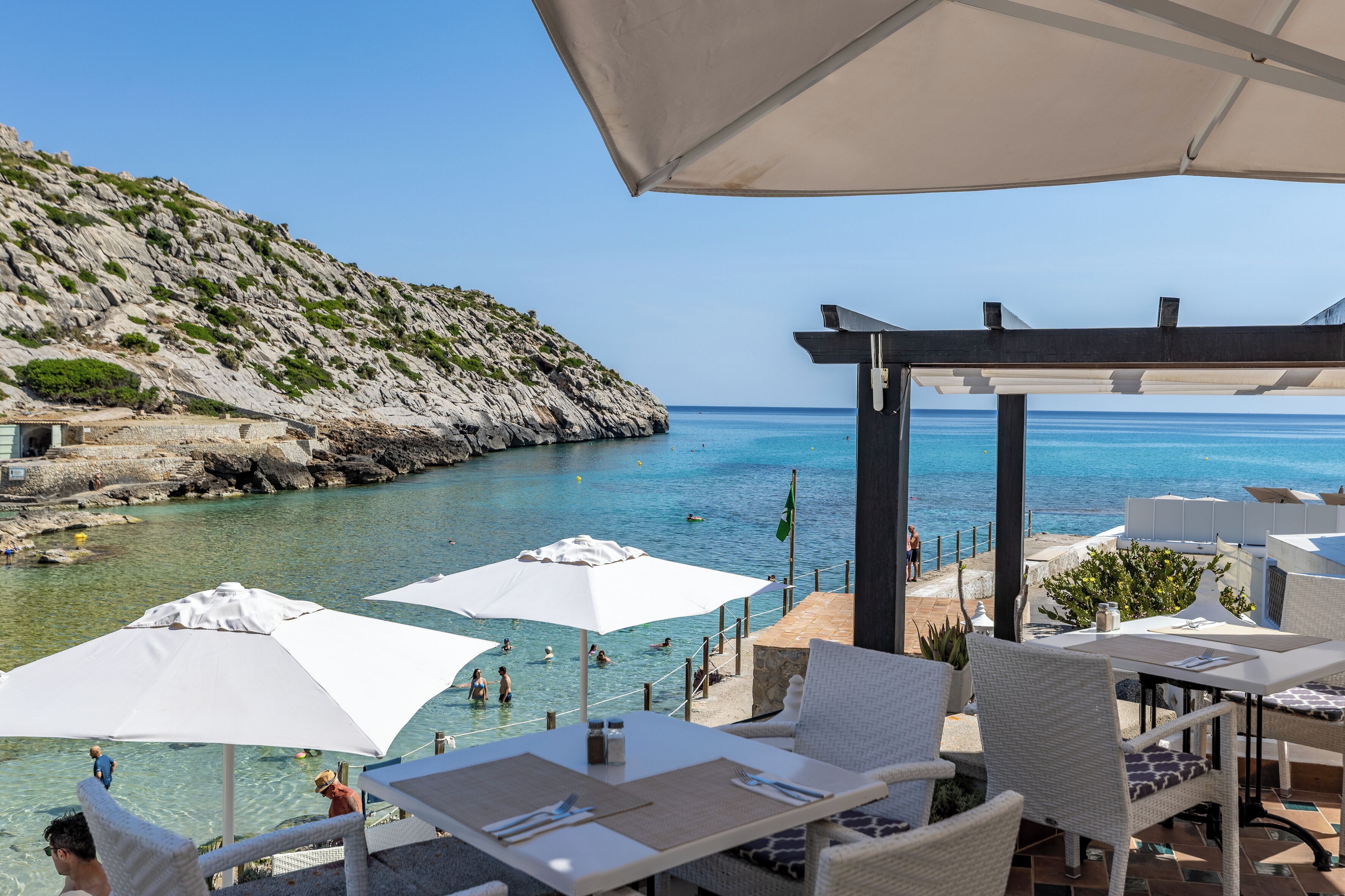 A seaside patio with outdoor seating, a view of the sea, and a rocky hillside.